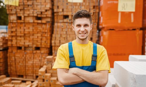 Male builder at the pallets of bricks in hardware store. Constructor in uniform look at the goods in diy shop